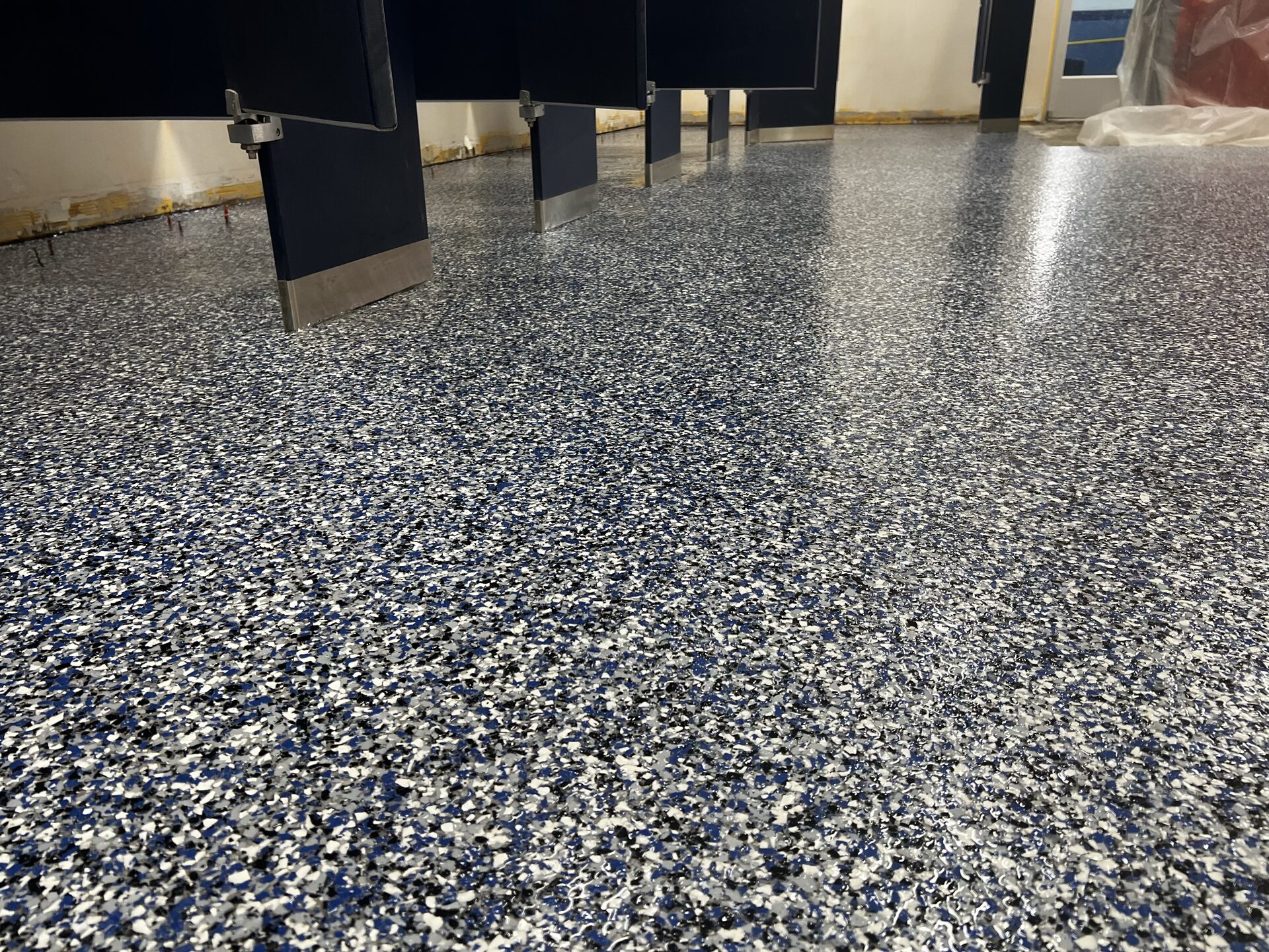 Detail of custom blue-and-white broadcast flake floor in swim school changing room with heavy grip additive in the polyaspartic topcoat